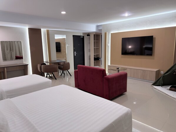 Habitación de hotel con dos camas, un sillón rojo, un televisor y un área de comedor con mesa y sillas.