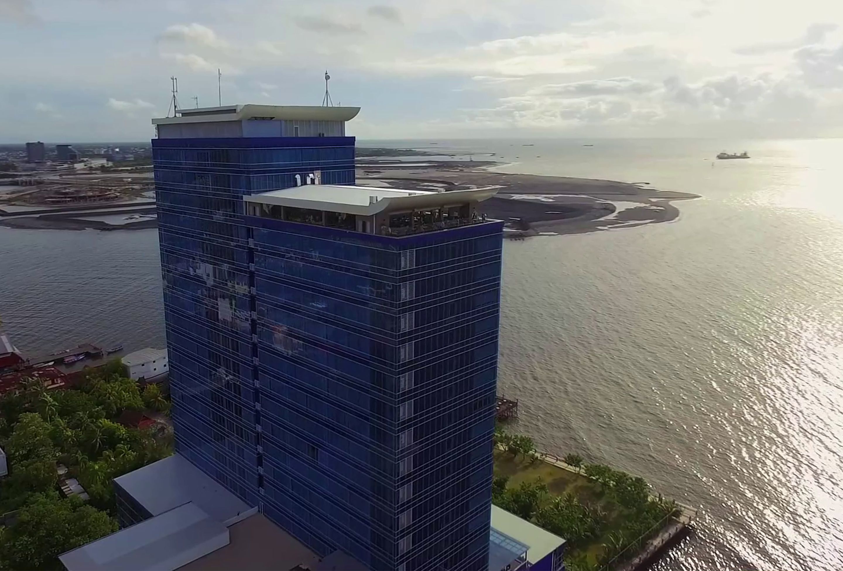 Un grattacielo con facciata in vetro moderno che si affaccia su una zona costiera con spiaggia e mare.