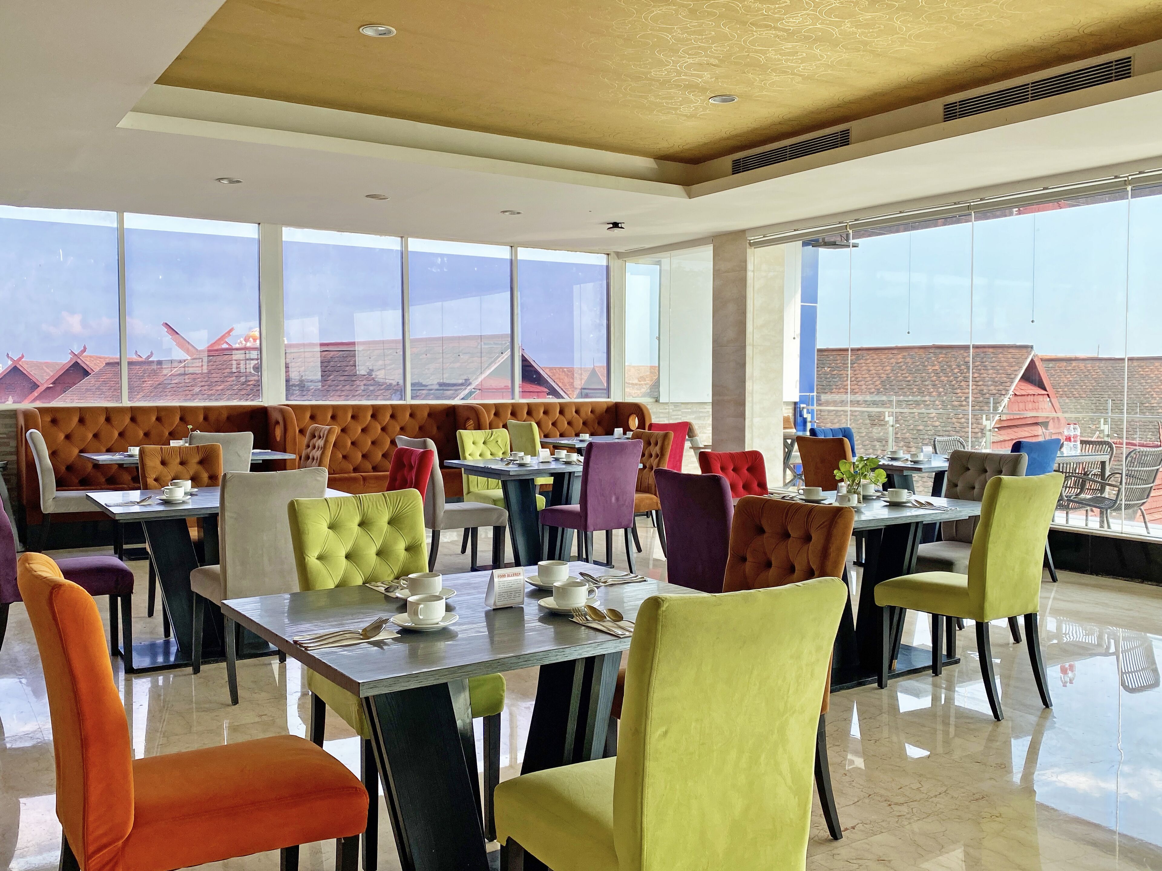 A modern dining area with high ceilings, large windows, and a variety of colorful upholstered chairs and tables.