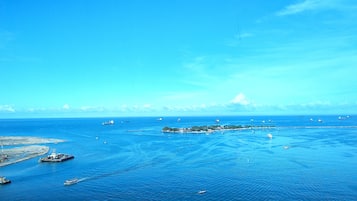 Vista aèria d'una zona costanera amb diversos vaixells i embarcacions a l'aigua, una petita illa amb edificis i un cel blau i clar.