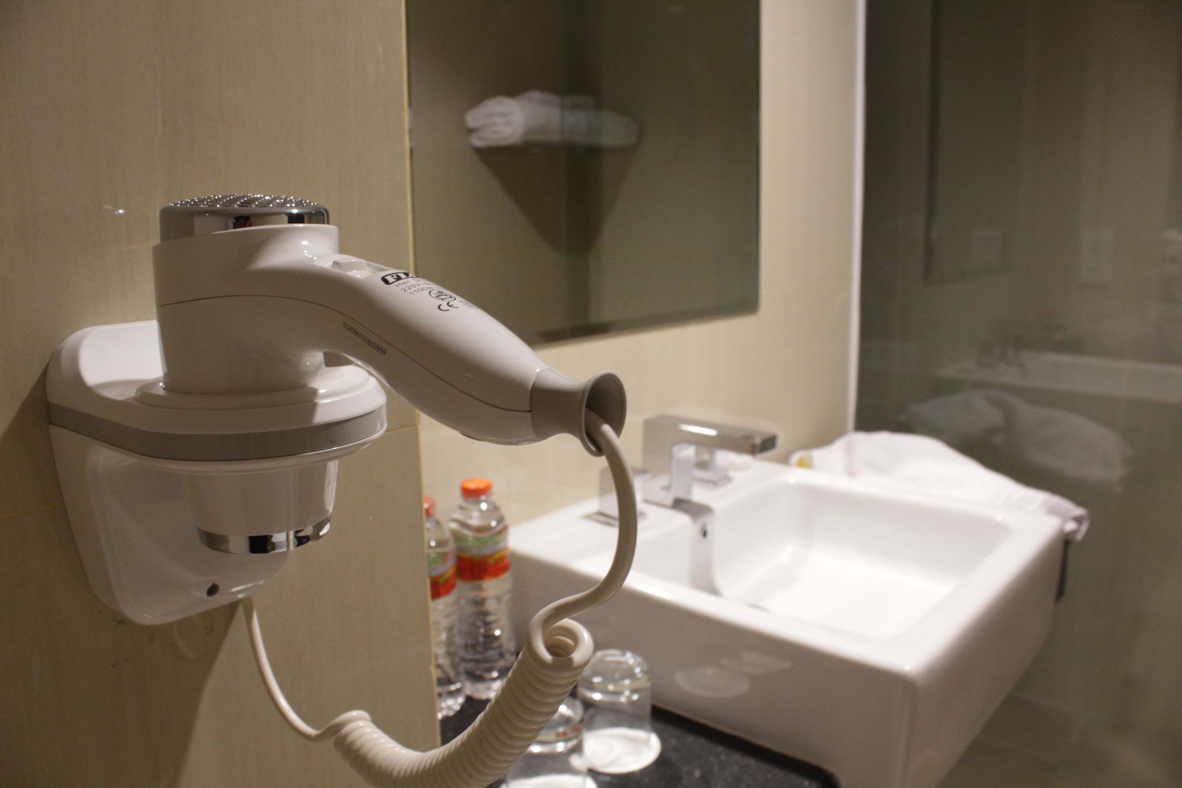 A bathroom with a hairdryer mounted on the wall, a sink, and a mirror.
