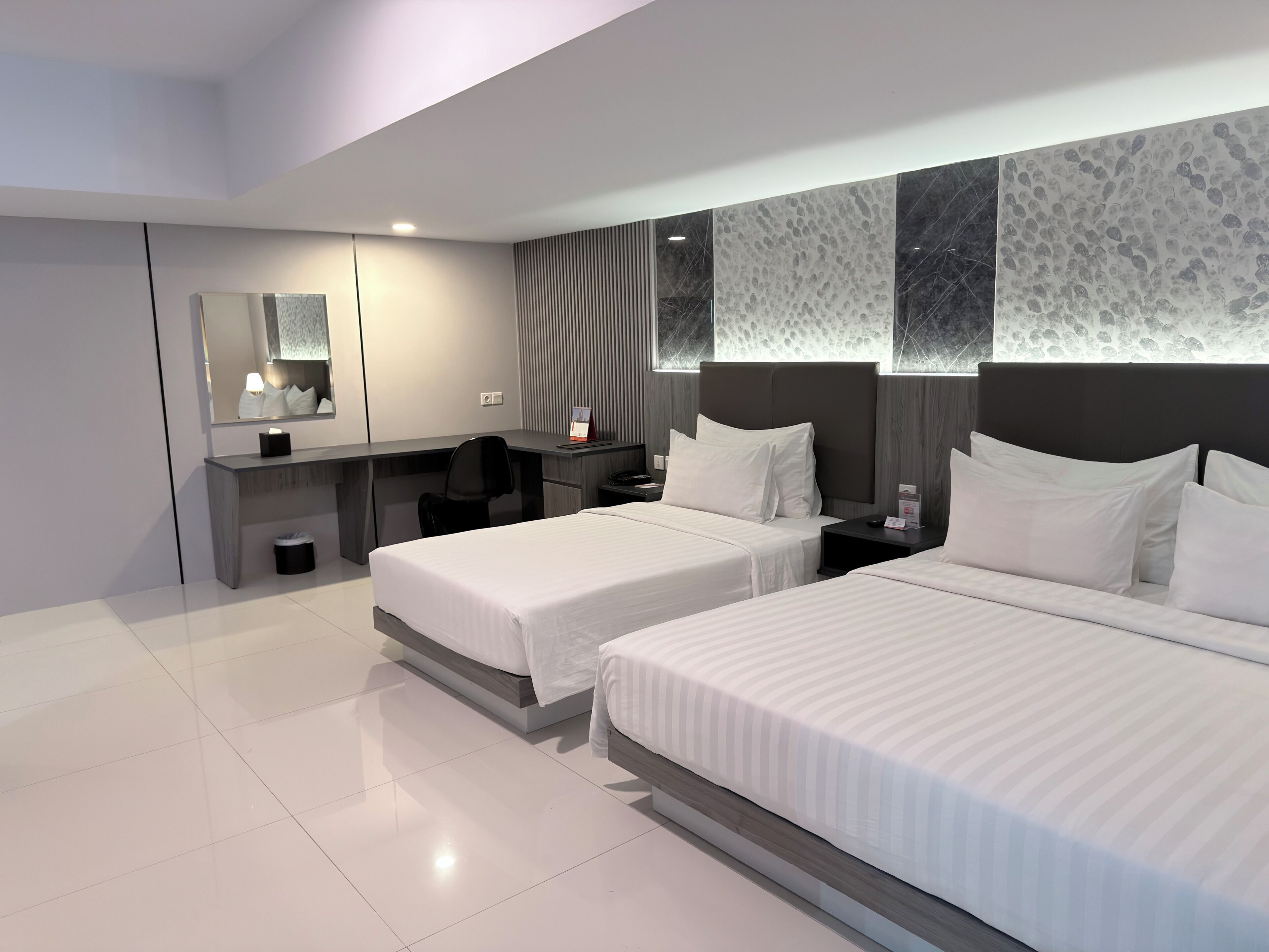A modern hotel room with two beds, a desk, a chair, and a large mirror.