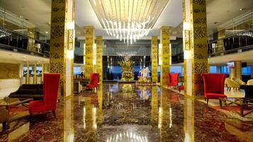 A spacious lobby with a polished marble floor, red armchairs, and a central floral arrangement.