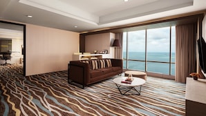 Une chambre d’hôtel moderne dotée d’une grande fenêtre donnant sur la mer, d’un canapé marron, d’une table basse ronde et d’un tapis à motifs.