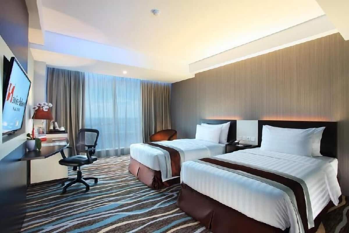 Habitación de hotel con dos camas, un escritorio, una silla y un televisor.