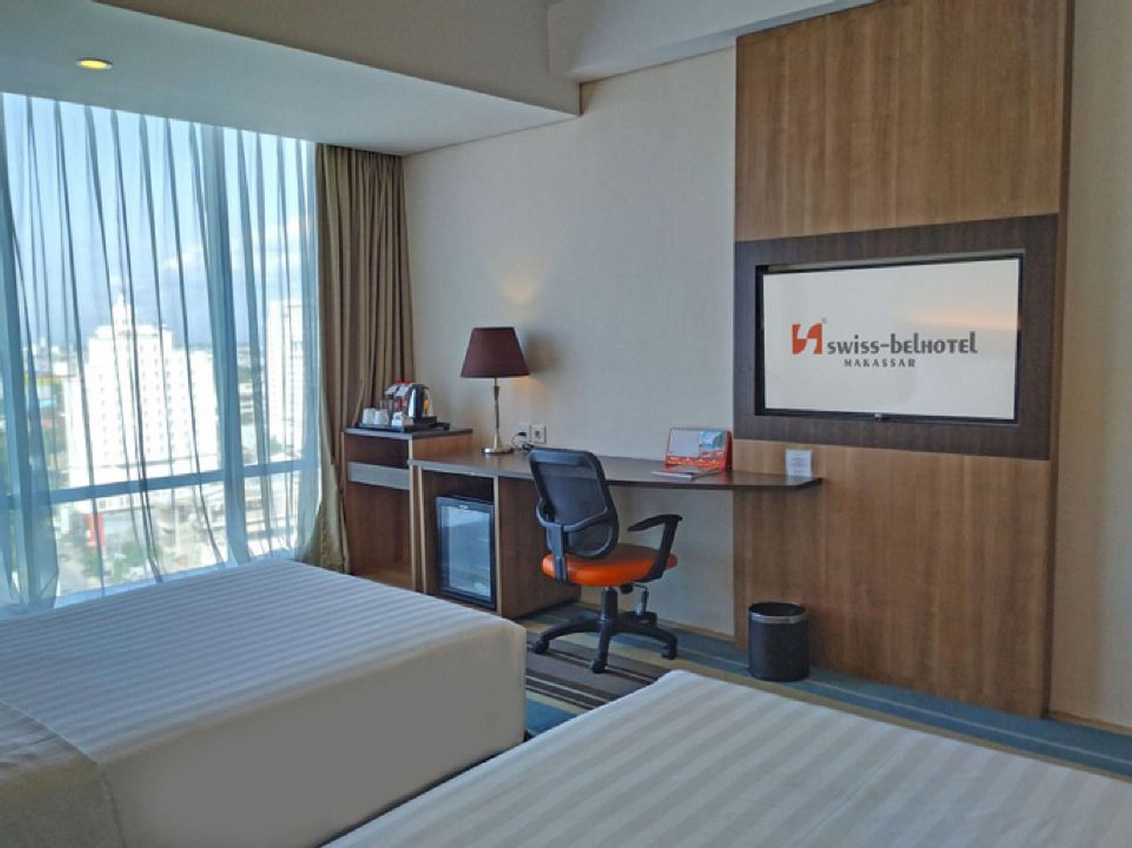 A hotel room with two beds, a desk, a chair, a TV, and a window with curtains.