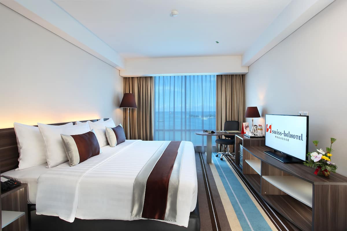 Habitación de hotel con cama, escritorio, televisión y vista a la ciudad.