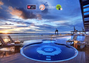A pool area with lounge chairs and a view of the sunset over the water.