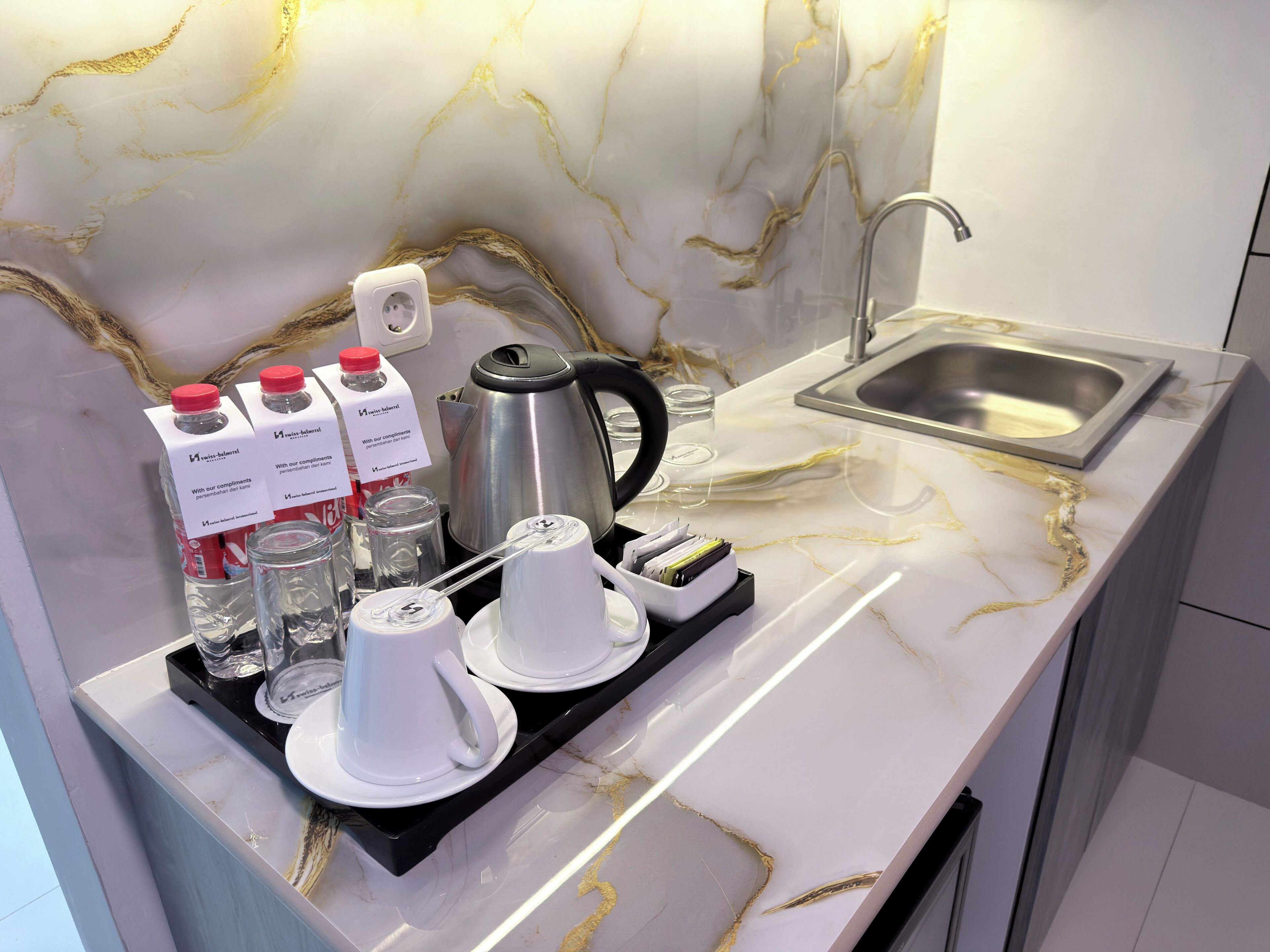 A modern kitchen with a marble countertop, a kettle, a coffee machine, and a tray with cups and bottles.