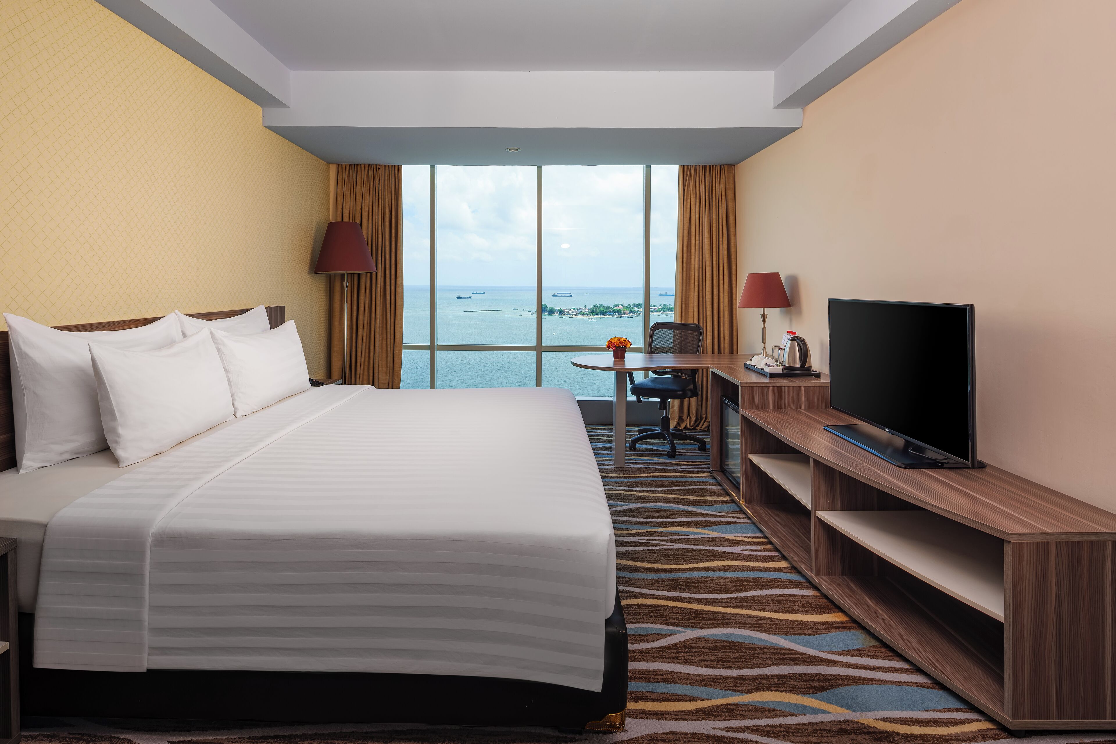 Habitación de hotel con una cama grande, un escritorio con televisor y vistas al mar.
