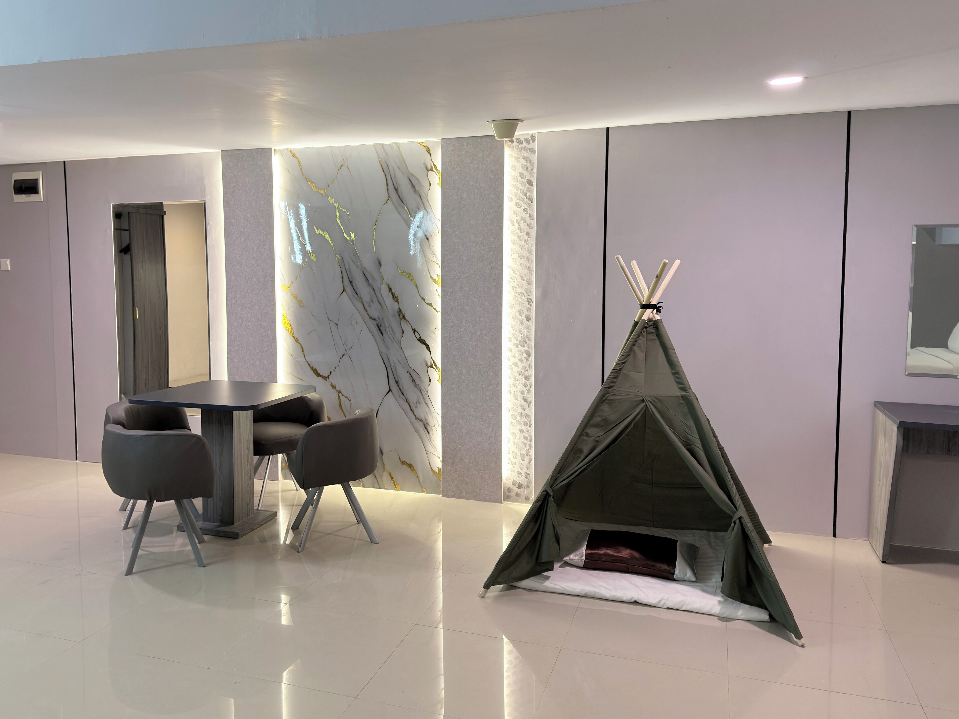 Une pièce moderne comprenant une table et des chaises, un mur décoratif orné d’un motif rappelant le marbre, et une structure en forme de tente tipi.