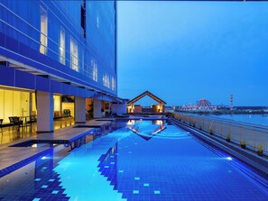 A modern hotel with a pool area, outdoor seating, and a view of a distant landmark.