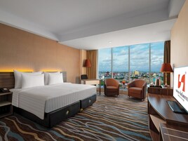A hotel room with a large bed, two armchairs, a desk, and a view of the city.