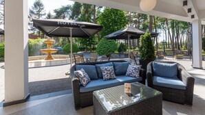 Een overdekt terras met rieten meubilair en parasols, waarop 