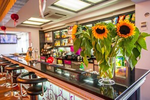 A bar area with a counter, stools, and a vase with sunflowers. - Hotel Jan (Darlowo)