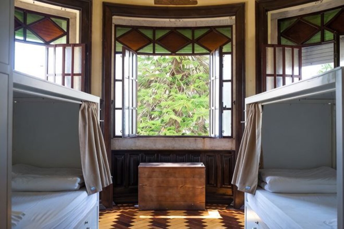 A room with two bunk beds, a bench, and a window with a view of greenery.