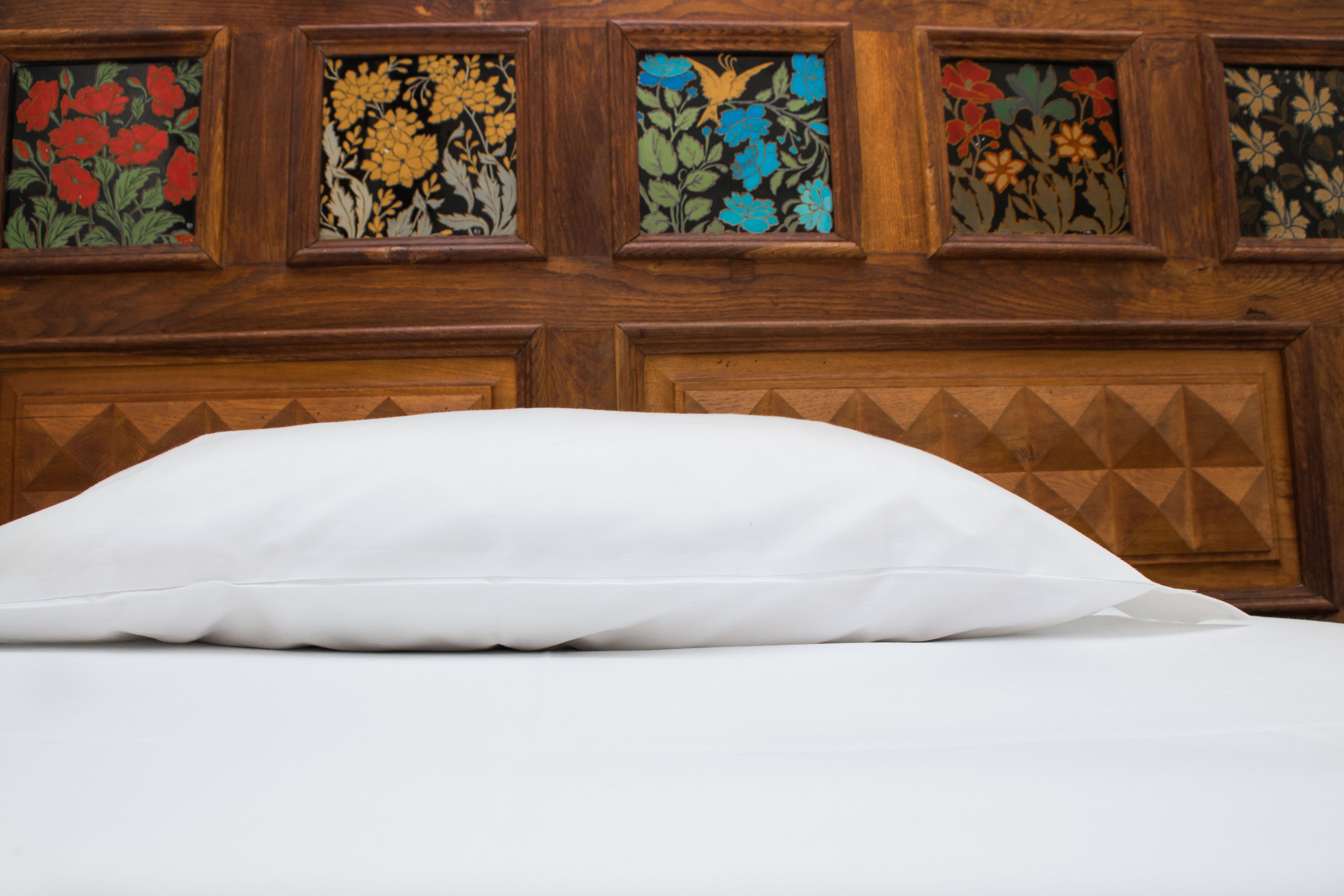 A bed with white bedding and a wooden headboard with floral stained glass panels.