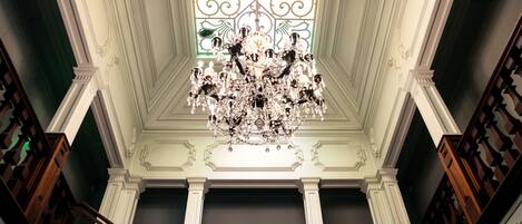 A grand staircase with a chandelier, ornate columns, and a decorative ceiling.
