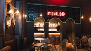 Un bar con un letrero de neón que dice "IMPERIAL BAR", con asientos en arco y una barra llena de botellas.