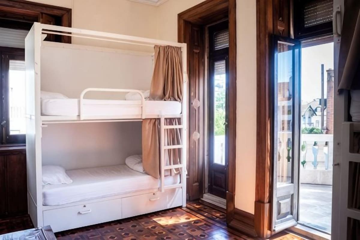 Un lit superposé avec une échelle, un petit tiroir et un rideau.