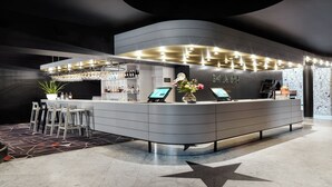 A modern hotel reception area with a curved counter, digital check-in kiosks, and a star-patterned floor. - MABI City Centre (Maastricht)