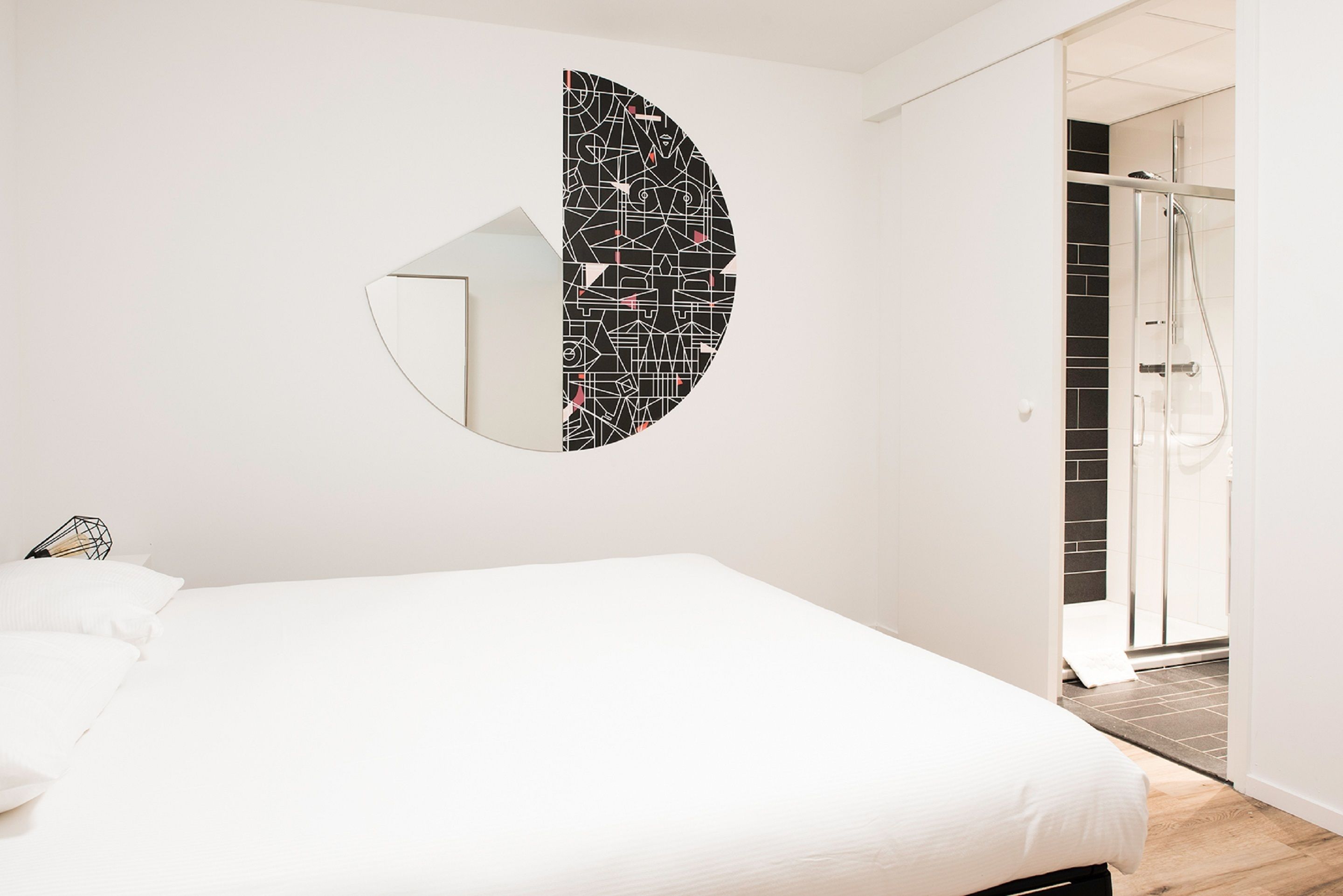 Een slaapkamer met een bed, een spiegel aan de muur en een douchecel zichtbaar door een open deur.