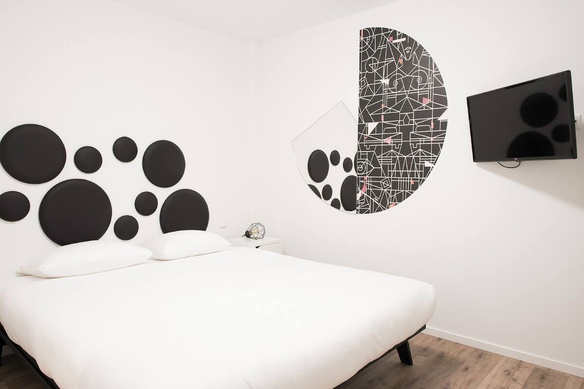 A modern bedroom with a large bed, a wall-mounted TV, and abstract wall art.