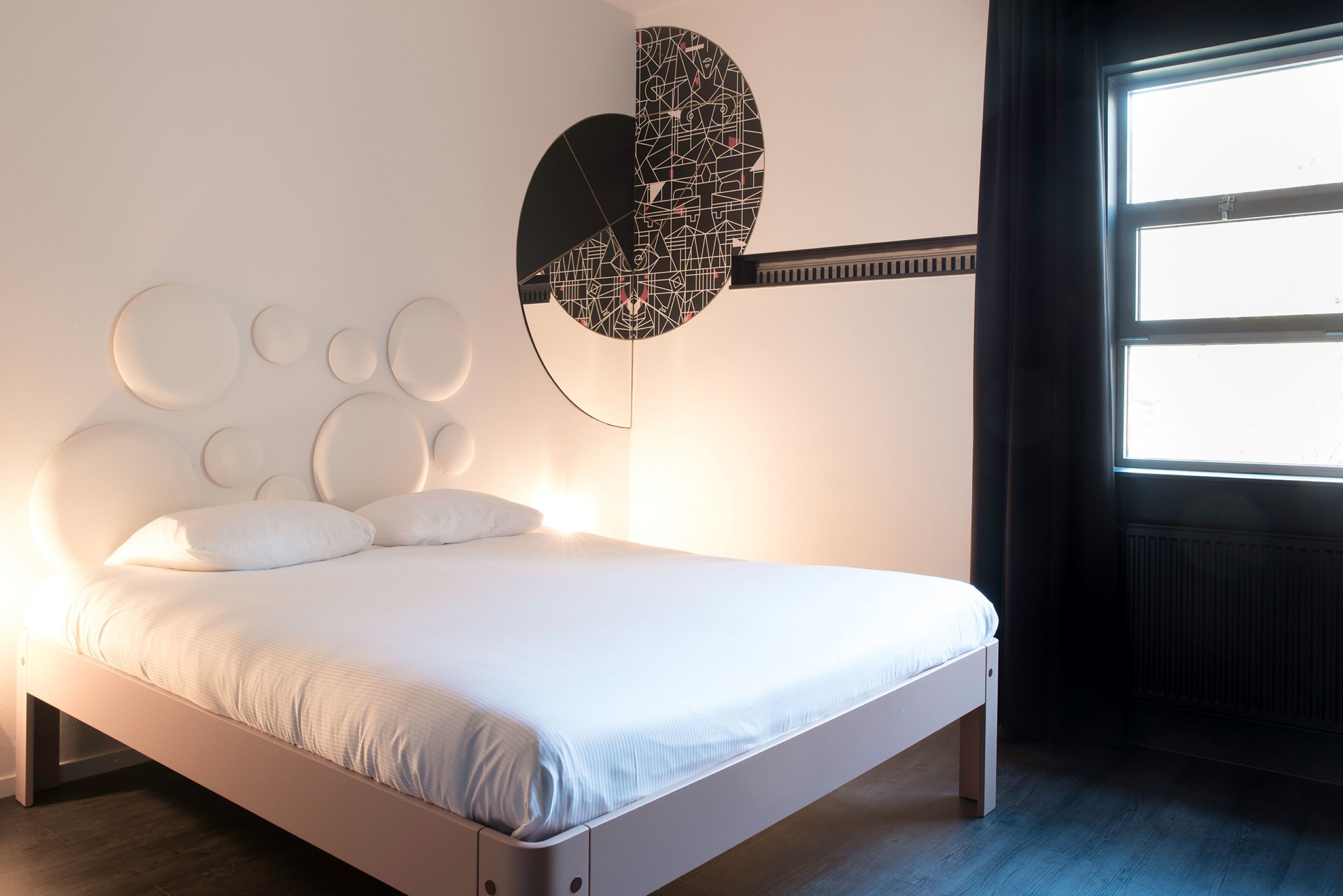 A modern bedroom with a white bed, circular wall decorations, and a unique wall-mounted guitar-shaped light fixture.
