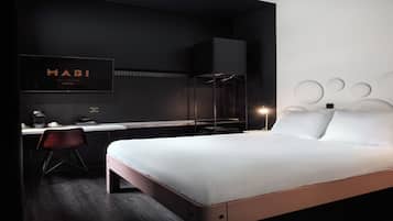 A modern hotel room with a bed, desk, chair, and a wall-mounted TV displaying the hotel name.