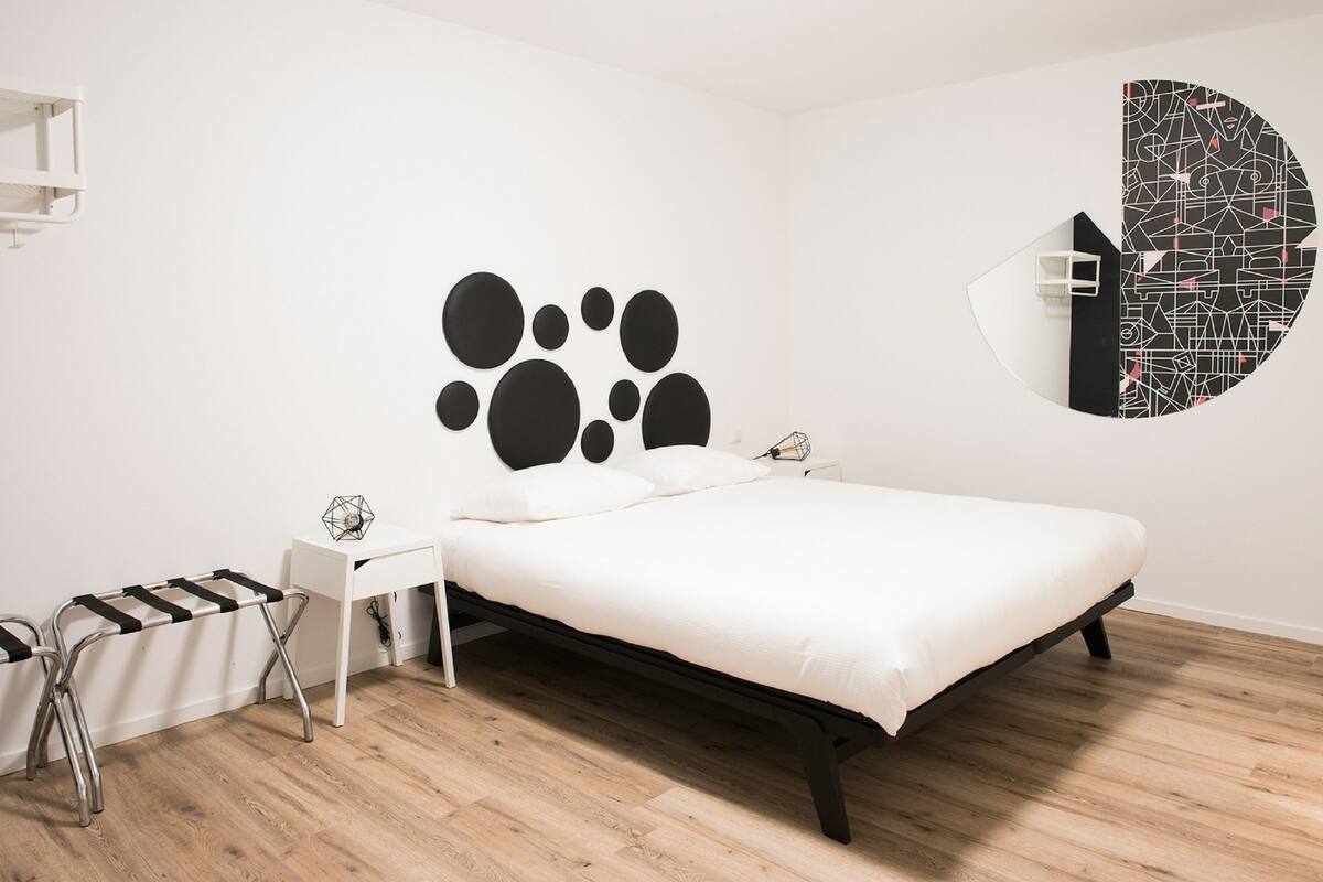 A modern bedroom with a bed, a white desk, and a wall-mounted mirror.