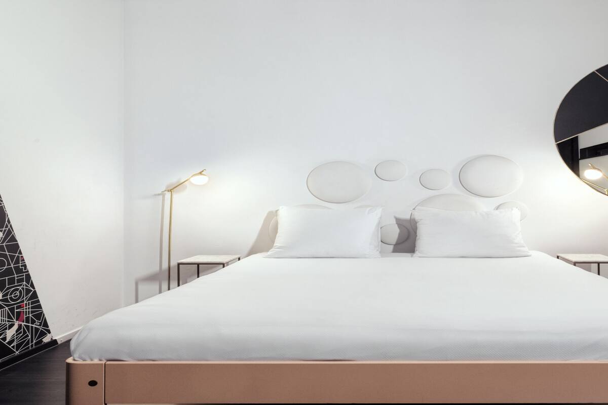 A modern bedroom with a large bed, two bedside tables, and a wall-mounted mirror.