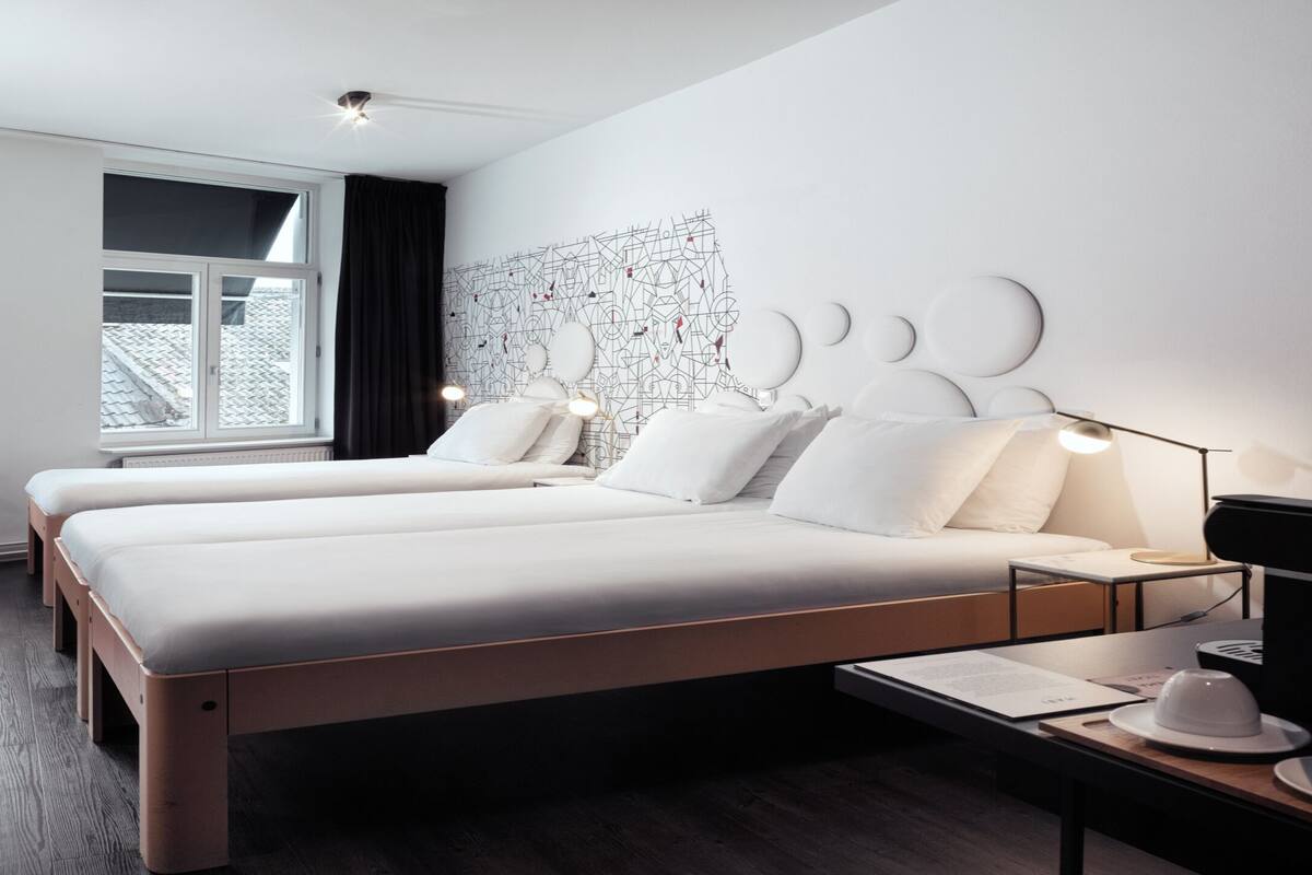 A modern hotel room with a large bed, bedside tables, a desk, and a chair.