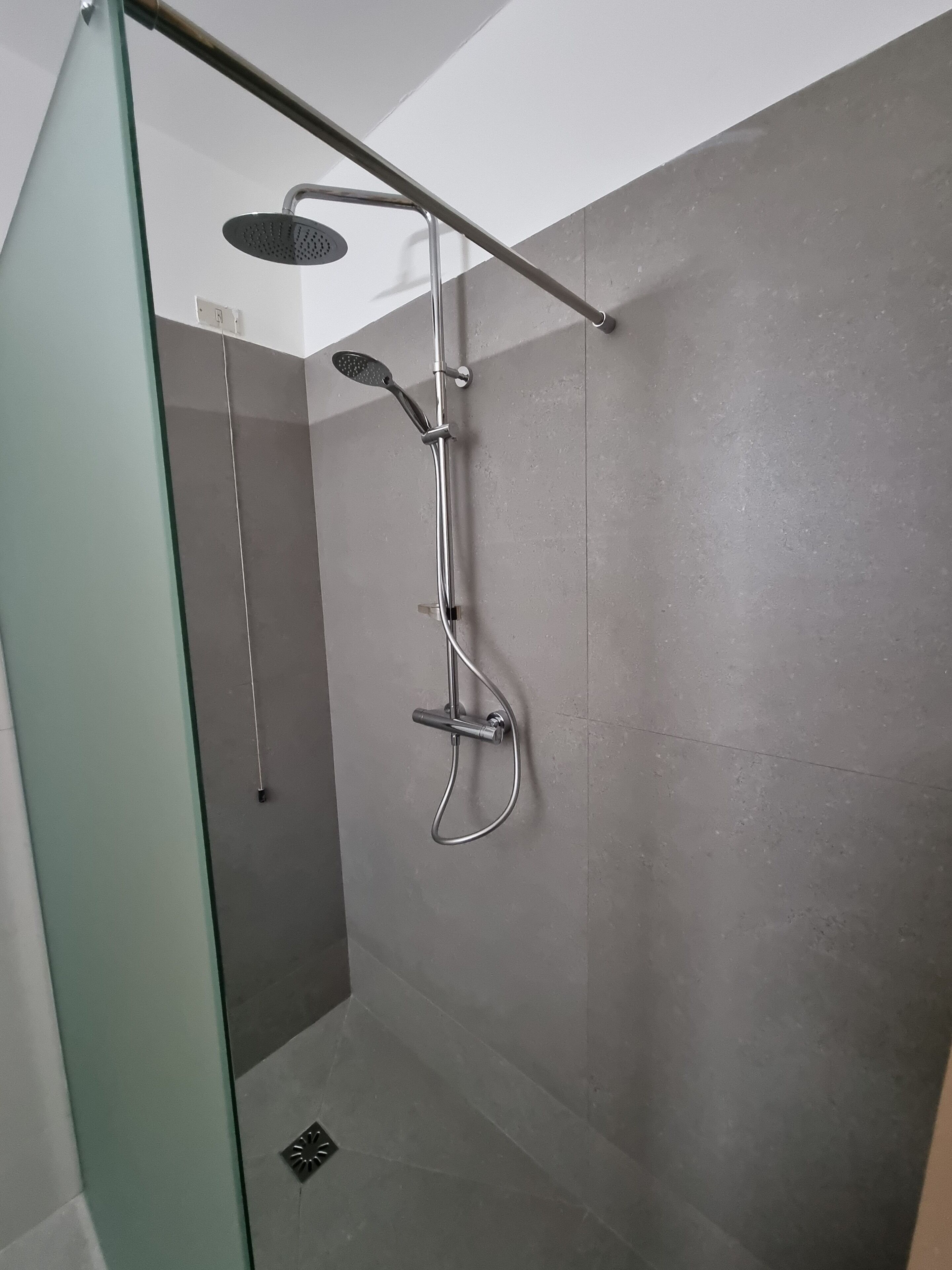 A modern shower with a handheld showerhead and a wall-mounted rain showerhead.