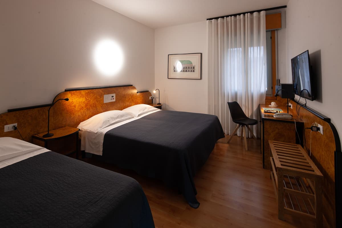 Habitación de hotel con dos camas, un escritorio, una silla, un televisor y un cuadro en la pared.
