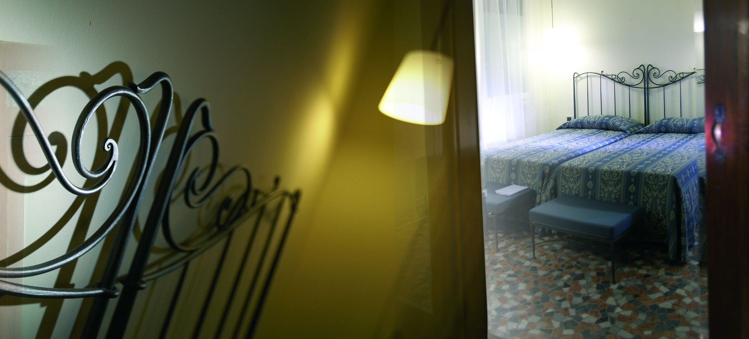 A hotel room with a metal bed frame, a bedside table, and a patterned floor.