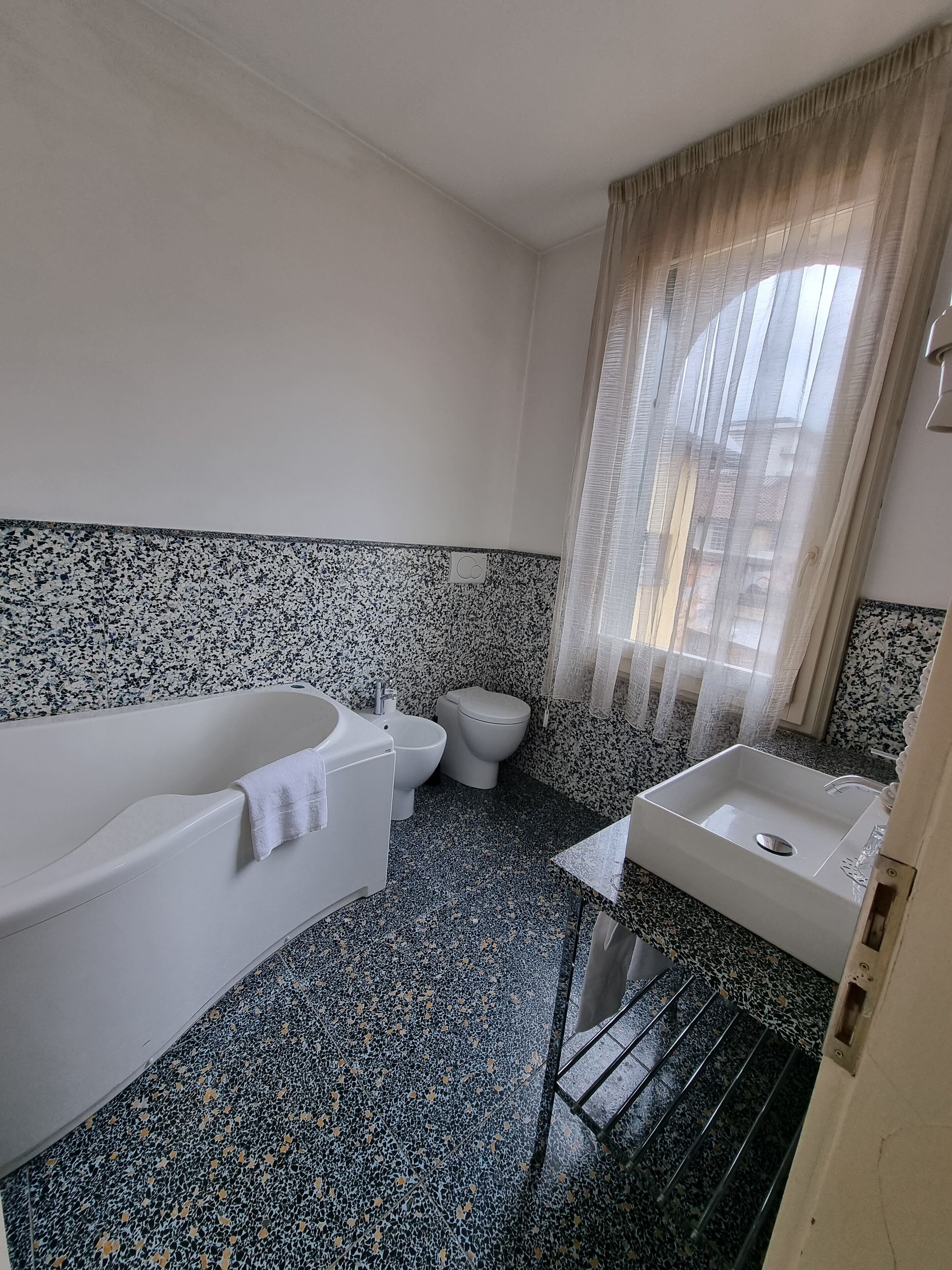 Un baño con una bañera blanca, un inodoro y un lavabo. El suelo presenta un diseño moteado.