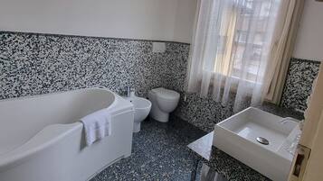 Un baño con una bañera blanca, un inodoro y un lavabo. El suelo presenta un diseño moteado.