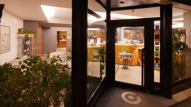 A hotel lobby with a reception desk, seating area, and a glass door entrance.