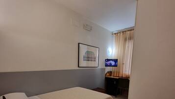 A hotel room with a bed, a desk with a computer, a framed picture on the wall, and a telephone on a small table.