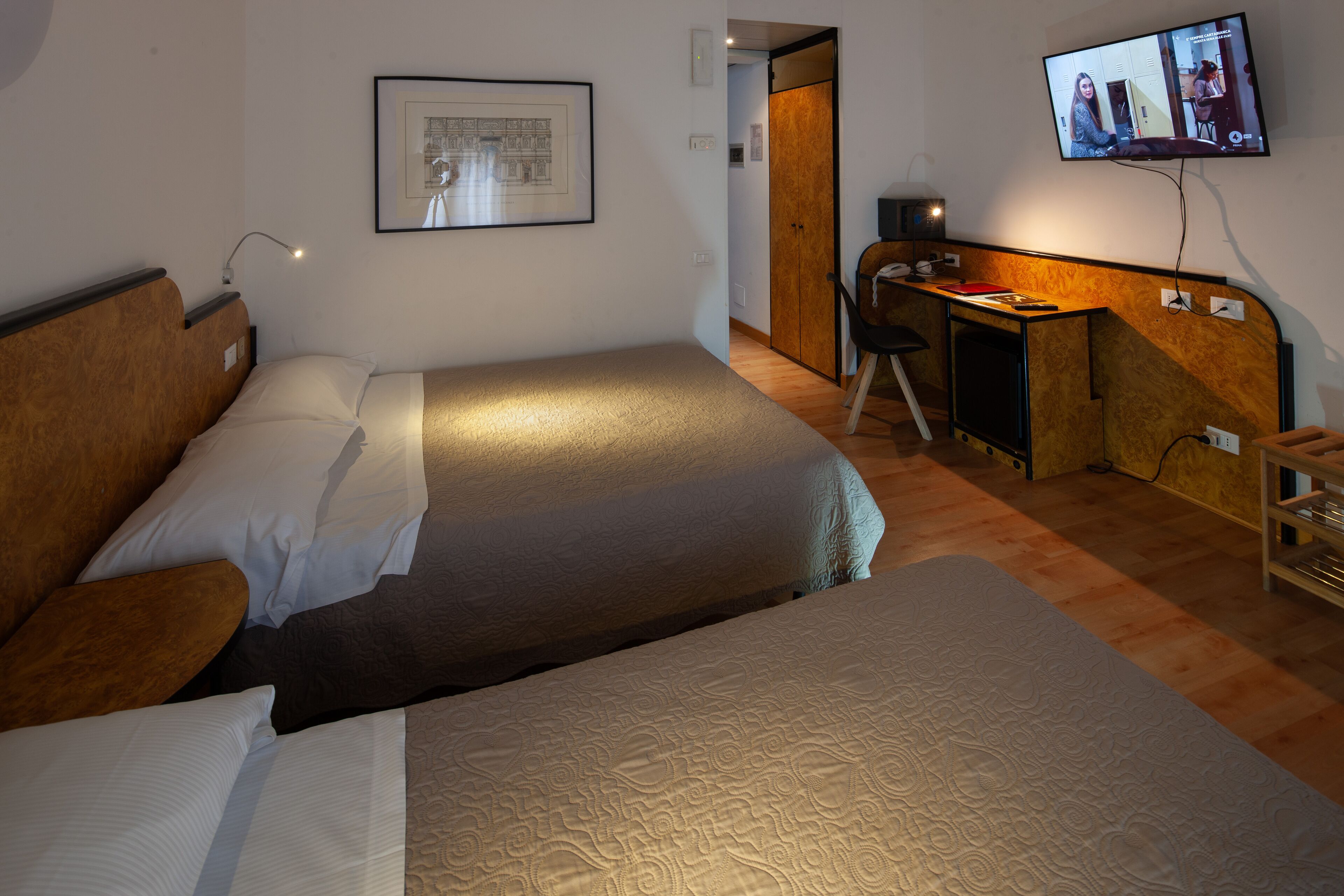 Habitación de hotel con dos camas, un escritorio, un televisor y un cuadro en la pared.