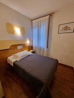 Una habitación de hotel con cama, mesita de noche, lámpara y un cuadro en la pared.