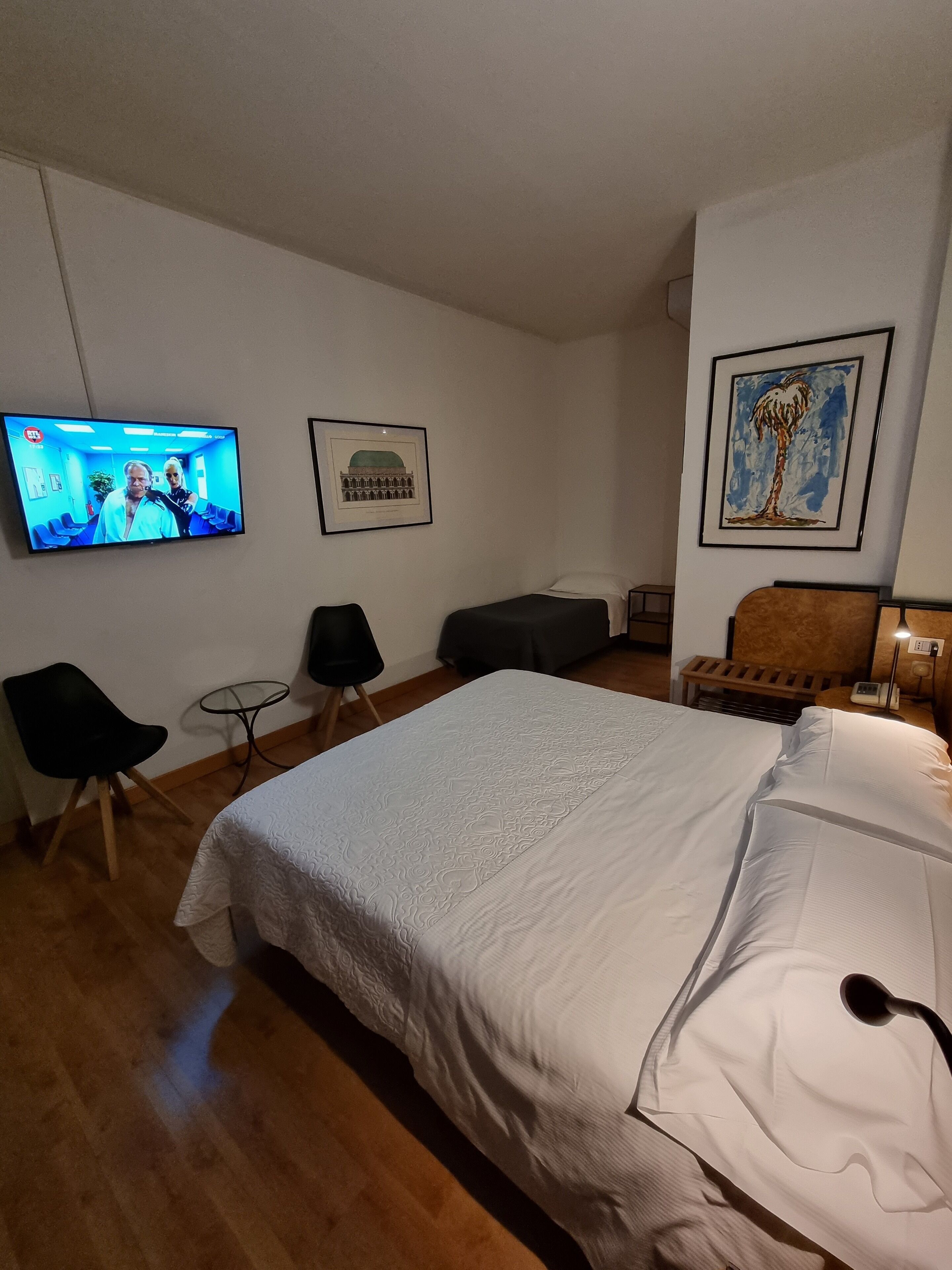 Habitación de hotel con una cama grande, un televisor montado en la pared, un cuadro enmarco y una mesita.