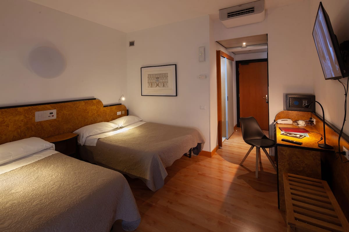 Habitación de hotel con dos camas, un escritorio con silla, televisor y un cuadro en la pared.