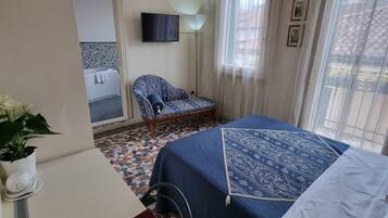 A hotel room with a bed, a chair, a desk with a computer, a TV, and a window with curtains.