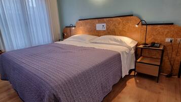 A neatly made bed with a purple blanket, a bedside table with a lamp, and a wall-mounted light fixture.