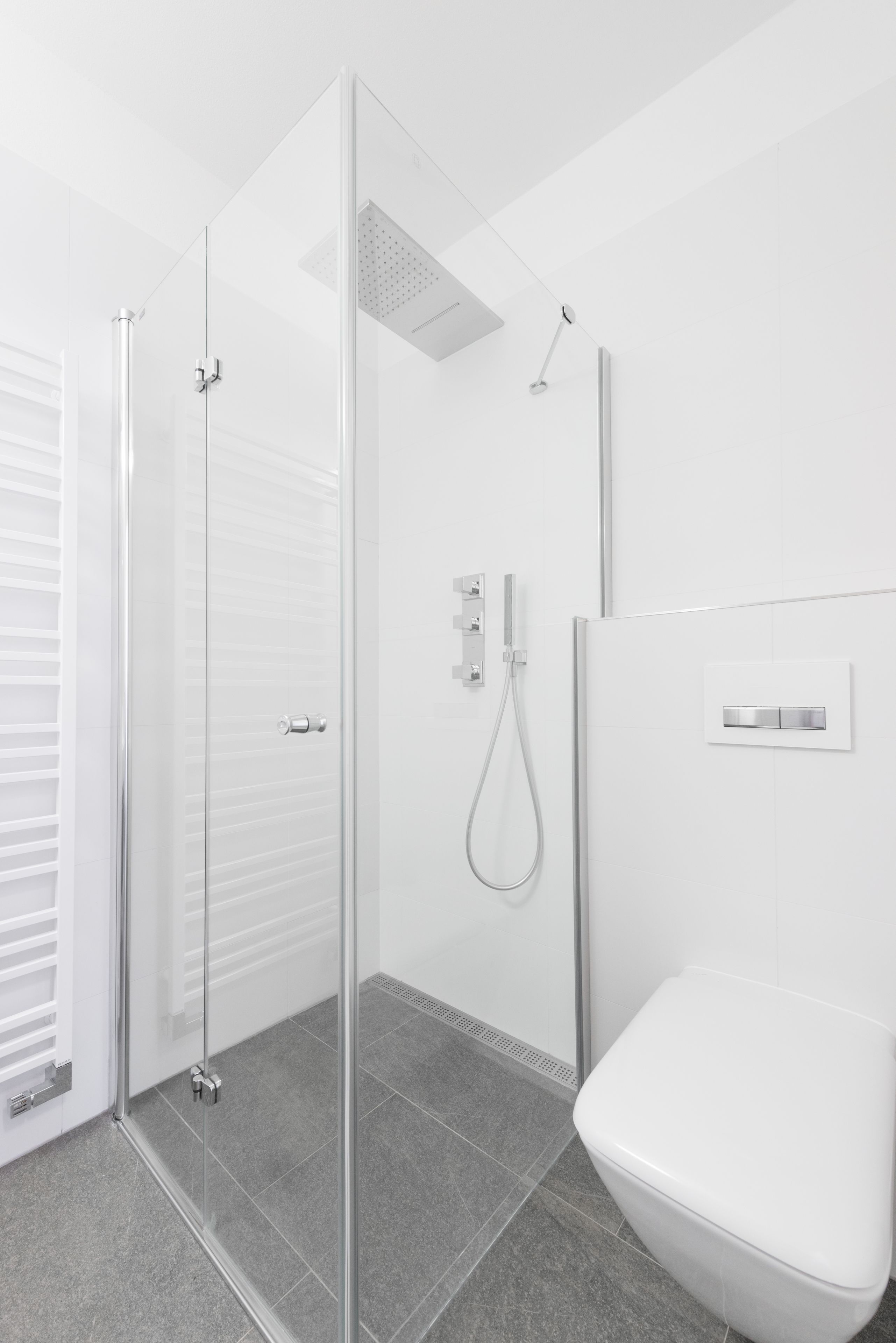 A modern bathroom with a glass shower enclosure, a toilet, and a wall-mounted control panel.