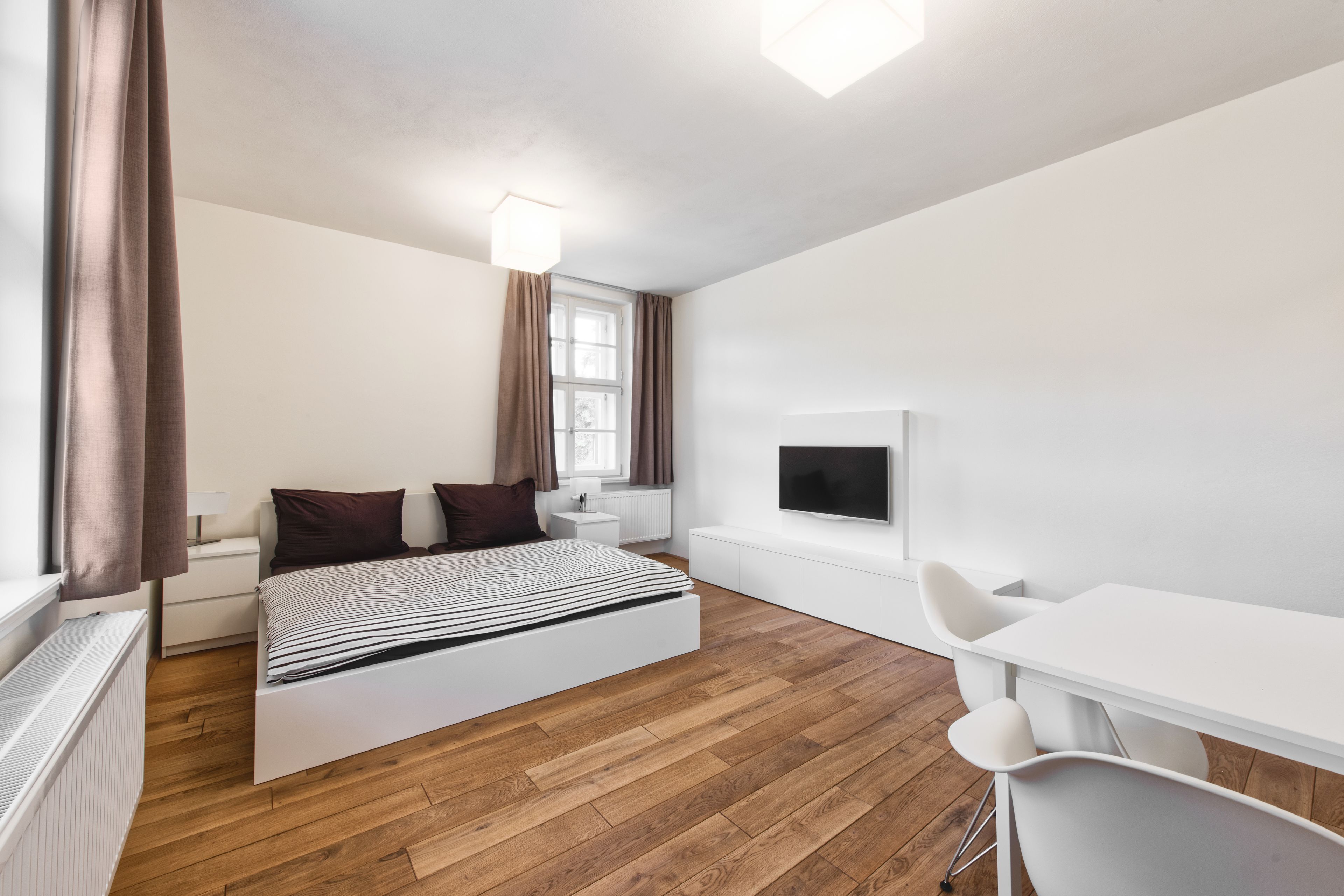 Een moderne slaapkamer met een bed, nachtkastje, lamp en een televisie.