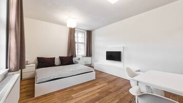 Een moderne slaapkamer met een bed, nachtkastje, lamp en een televisie.