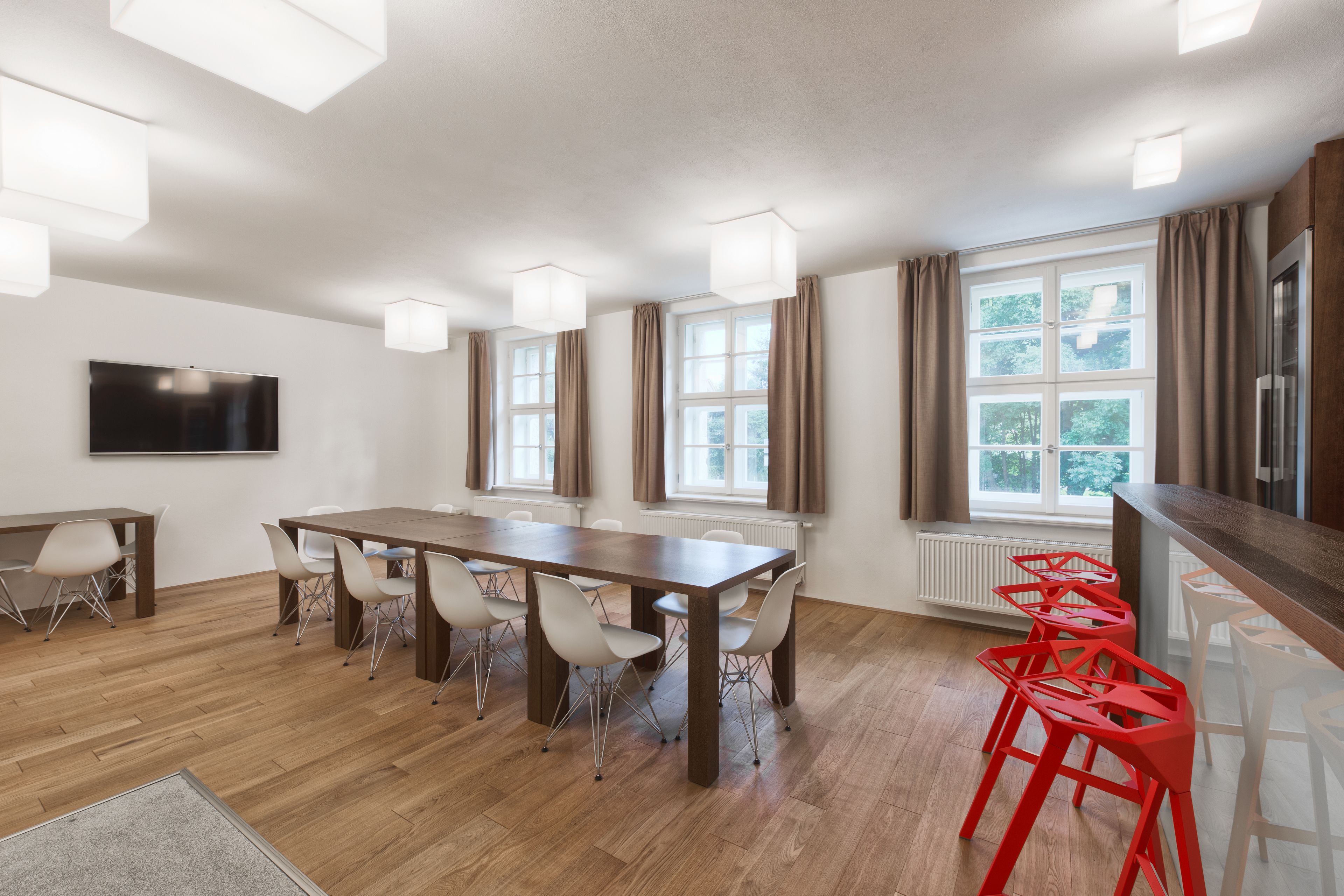 Een moderne keuken met een houten tafel, witte stoelen en rode barkrukken.