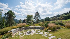 A stone fire pit surrounded by a stone wall, with a grassy area and trees in the background. - Theresian Apartment (Ostruzna)